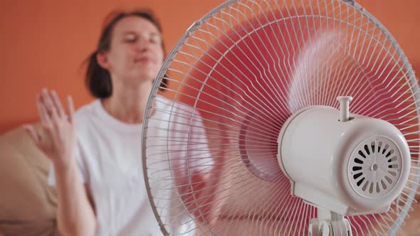 Young Woman Sits in Front of Electric Fan Waving Hands Air Stream Blowing Hair