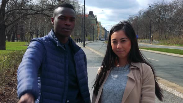 A Young Black Man and a Young Asian Woman Show Thumbs Down To the Camera in a Street