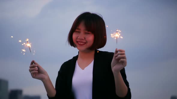 Happy asian women enjoy and play sparkler at roof top party at evening sunset.