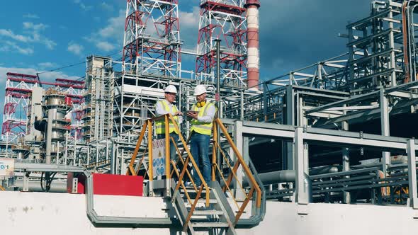 Oil Refinery Premises with Two Engineers Having a Discussion