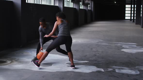 African american man and woman standing in an empty building playing basketball