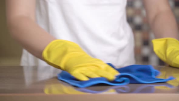 Women's hands in the protective gloves cleaning the surface of the kitchen countertop.