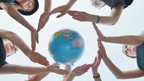 Schoolgirls Hug the Earth Globe with Their Hands Making a Circle Out of Them on the Background of