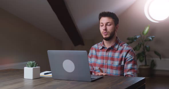 Young Man Talking with Partners Via Video Chat on Laptop Sitting at Home Office Slow Motion