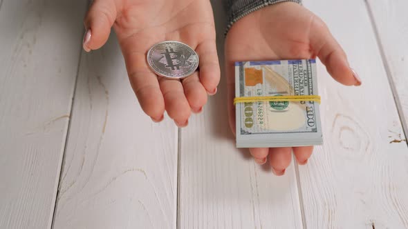 Closeup of a Bitcoin and a Stack of Hundred Dollar Bills in the Hands of a Woman