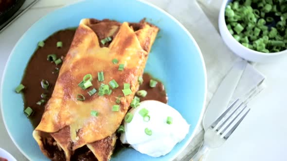 Dinner plate with Chicken enchiladas garnished with green onions and sour cream.