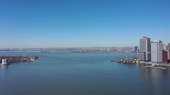 An aerial view the east East River on a sunny day with blue skies. The drone camera, facing lower Ma