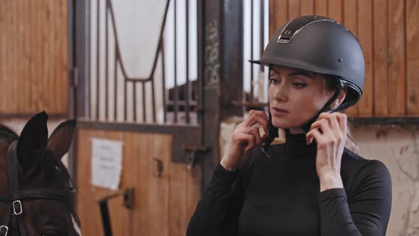 A Woman Puts on a Plastic Helmet Standing Near the Horse