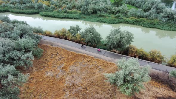 Couple ride bicycles along a riverside nature trail - aerial follow view