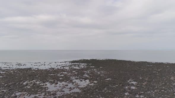 Wide aerial tracking out over pebbly beach to the expanse of wide open water on the coast of Exmoor,