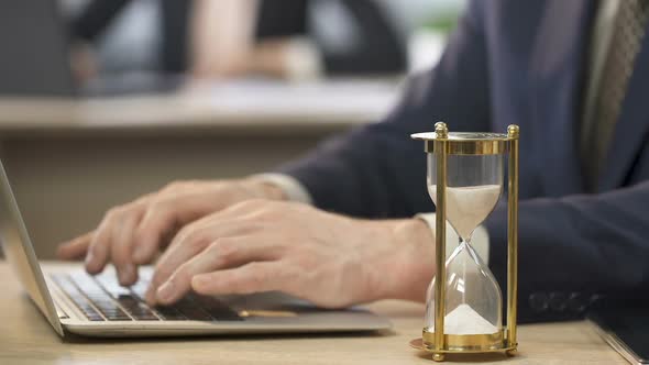 Man in Suit Working on Laptop at Office, Hourglass Standing on The Table, Time