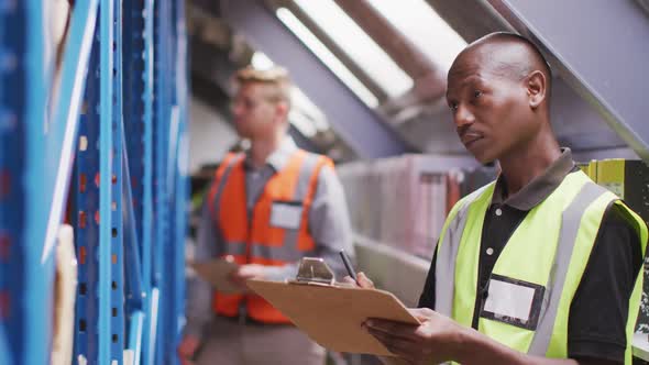 An African American male factory worker at a factory making hydraulic equipment taking notes