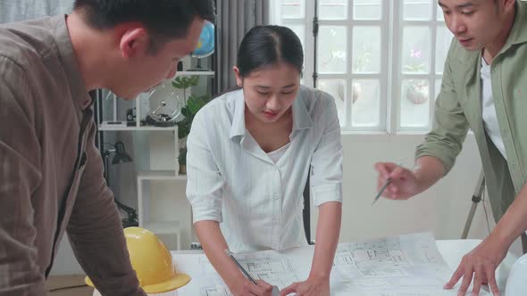 Group Of Asian Engineers Helping Each Other Drawing Building Construction At The Office