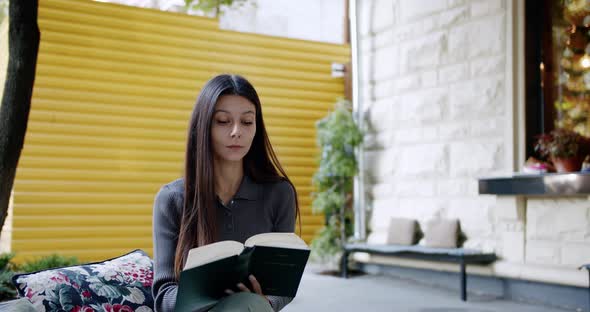 Smiling Young Woman is Reading Interesting Book Outdoor Leafing Through a Book alt