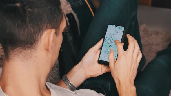 Man Looking at Map With Marked Points on Smartphone While Lying on Couch in Room