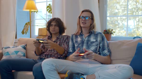 Young Cheerful Guys Playing on Console Sitting on Couch at Home
