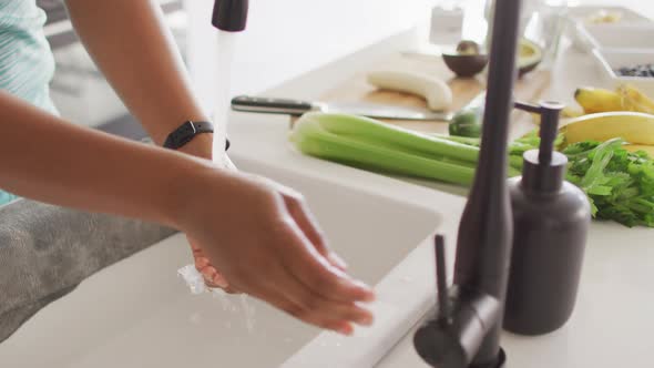 Midsection of african american woman washing hands in sink in kitchen