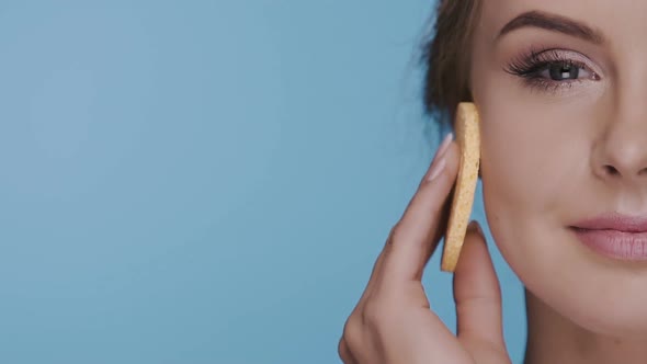 Close-up of Half Woman Face Removing Make-up with Sponge on Blue Background