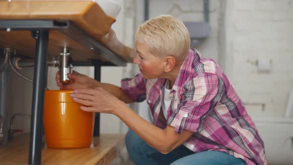 Senior Woman Fixing Leaking Sink Pipes in Home Bathroom