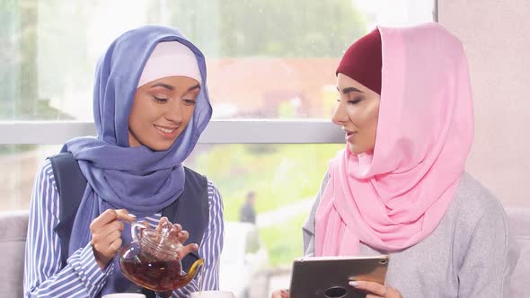 Beautiful Modern Muslim Women Communicate and Drink Tea in Coffee Shop