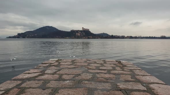Seagulls fly away from pier overlooking Maggiore lake and Angera fortress. Slow motion
