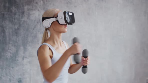 Young and sporty girl in sportswear is doing exercises at home using virtual reality helmet.