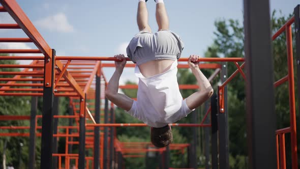 Young Male Gymnast Spinning on Gymnastic Bar on Sunny Day
