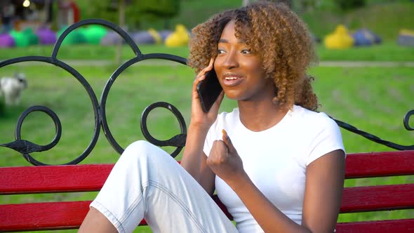 Happy African Woman Talking on the Phone While Sitting on a Bench in the Park