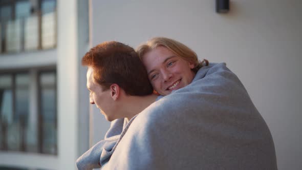 Lovely gay couple hugging on the balcony under a blanket