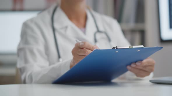 Close Up of Doctor Filling Patient History List in Clipboard Sitting in Hospital Office.