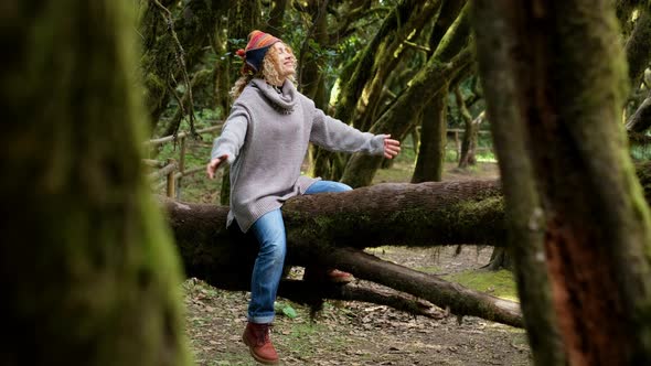 Happy adult female sitting on a trunk tree in forest woods enjoy wild nature park outdoors