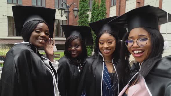 Happy University or College Graduates in Master's Gowns and Square Hats are Lively and Take Selfies