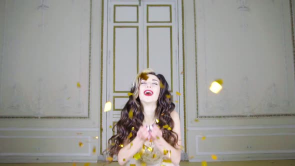 Young Brunette Woman with Red Lips Blows Gold Confetti