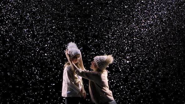 Joyful Smiling Mom and Little Girl Rejoice at the First Snow. Happy Family in the Studio on a Black