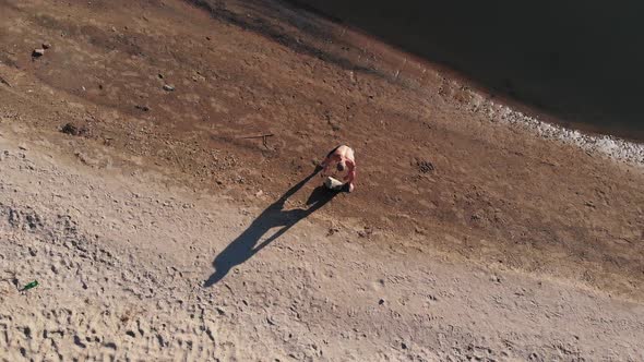 Young Man Walking on the Beach and Lifting a Big Heavy Stone