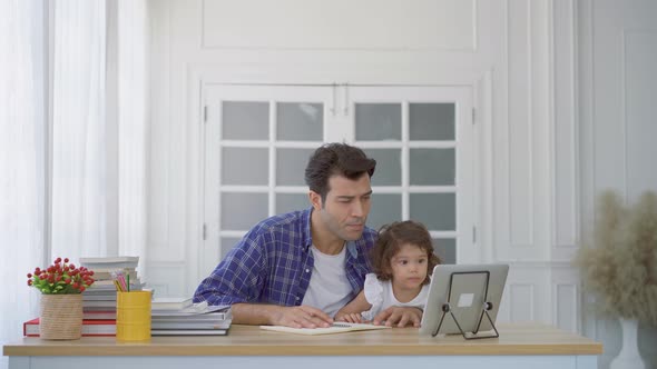 Father and little cute daughter watching the video tutorial on the tablet and teaching homework 