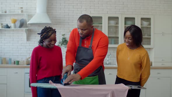 Caring Black Father Teaching Cute Teenage Daughters Ironing