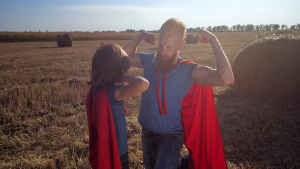 Dad and Son As Superheroes Showing Biceps Outdoors