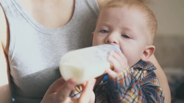 Mother Feeds Baby with Milk From Bottle in Spacious Room