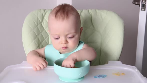 a Little Boy Touches Food with His Hands While Sitting in a Child's Chair