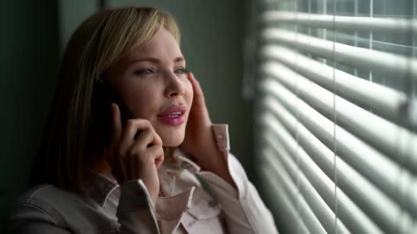 A Focused Woman Stands at the Window and Talks on the Phone, Works As a Customer Service Operator at