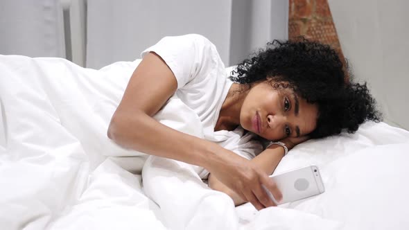AfroAmerican Woman on Smartphone Browsing Email and Messages Lying in Bed on Side
