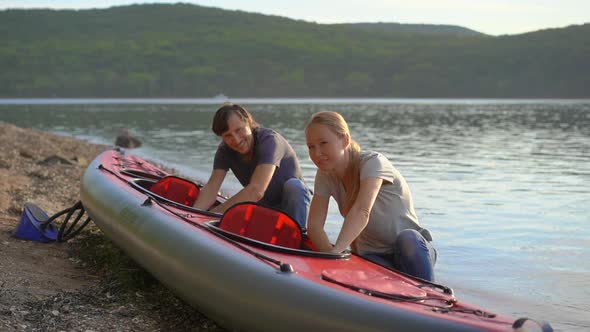 Young Man and Woman Prepare Their Inflatable Kayak for Paddling in a Lake or Sea. Slowmotion Shot