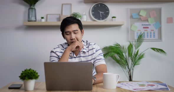 Tired sleepy Asian businessman closing computer laptop and laying head on arms