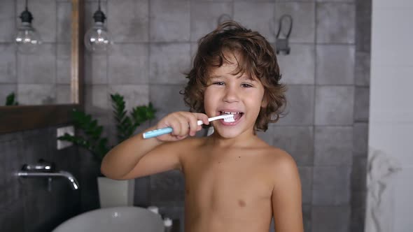 Boy with Curly Hairs in White Towel Brushing His Teeth Using Toothpaste