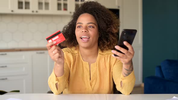 Excited Young AfricanAmerican Woman Holds Smartphone and Credit Card