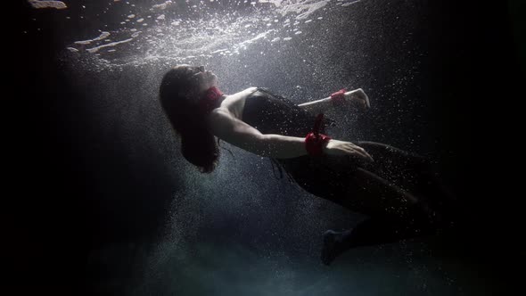 A Darkhaired Woman in Red Handcuffs Swims Deep Under the Water on a Dark Background She Soars