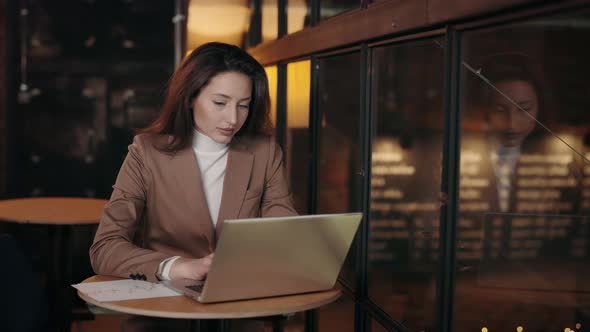 Woman Sitting at Cafe with Documents and Typing on Laptop