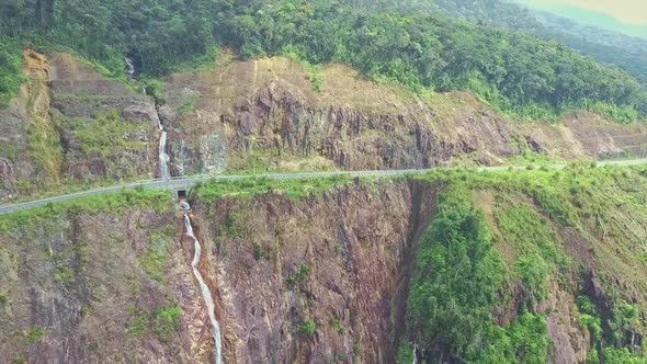 Drone Flies High Above Highway on Steep Cliff with Waterfall