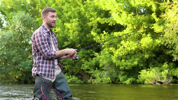 A Fisherman Throws a Fishing Rod Standing Kneedeep in the Water of the River